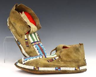 A pair of turn of the century Native American beaded moccasins, possibly Cheyenne.  Multi-color beadwork with geometric design on tanned hide with raw hide soles.  Some wear, lacks some ties, left with small loss to beadwork.  Up to 9 1/4" long.  
