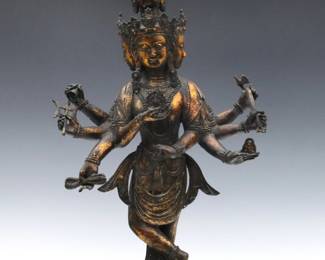 A Tibetan patinated Bronze figure of a Buddha.  Depicted with five faces and eight arms, standing on a lotus base.  Minor wear to patina.  26" high.  
