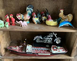 Top shelf: Chinese kissing couple, Royal Copley roosters, Dolphin paperweight. Lower shelf: Texaco ship, Harley Davidson motorcycle telephone
