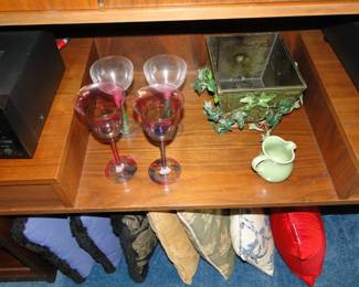 Pillows on the floor, neatly organized, and some other random items on the shelf