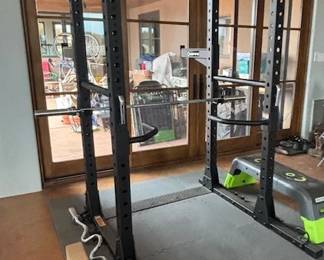 Workout room, which includes a power rack cage, weights, power bars, resistance bands, kettlebells, dumbbells, a treadmill, benches, and essential stretching equipment.