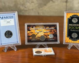 This lot features a variety of collectible coins including a slabbed double dated nickel from 1938, a 1986 S 50 cent coin PR65 by AACGS, an encased Sacagawea Dollar coin, & a three-coin slabbed collection of, “Collector’s Favorite Rare Coins” including an Indian Cent, Liberty Nickel, & a silver mercury dime.