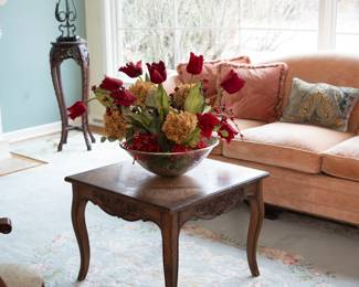 An antique square carved wooden coffee table with cabriole legs, with a glass bowl of silk flower arrangement