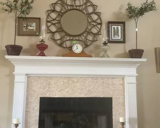 A view of the mantle and the beautiful round metal mirror among other items and a mantle clock.