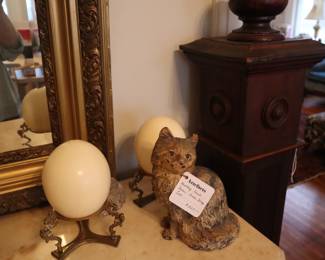 On the marble top of the chest, two ostrich eggs and an iron door stop, collectible persian cat. To the right an antique architectural newel post in the front entrance room.