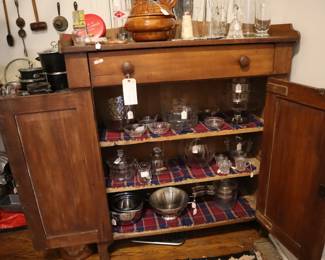 Another kitchen cupboard, more primitive, filled with kitchen tools; in the kitchen.