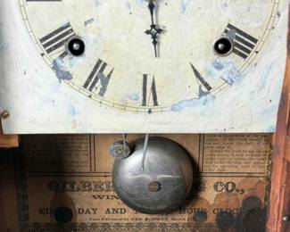 Antique Gilbert 8-day wooden case clock, chimes on the hour.  Cold painted face featuring roman numerals and front screen with reverse painted glass panel.  Includes key and pendulum.