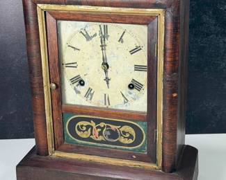 Antique Gilbert 8-day wooden case clock, chimes on the hour.  Cold painted face featuring roman numerals and front screen with reverse painted glass panel.  Includes key and pendulum.