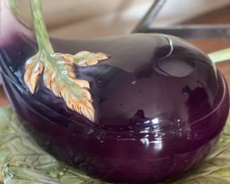 The image depicts a Fitz and Floyd Eggplant Tureen of the "Vegetable Garden" collection.
It is a serving dish, specifically a tureen, designed to serve soups or stews.
The tureen is shaped and painted to resemble an eggplant, complete with a leafy handle and base.
It was produced by Fitz and Floyd, a company known for its decorative ceramic pieces.
This particular design is from the late 20th century.
It is made of earthenware.
It is a discontinued piece, making it potentially collectible.