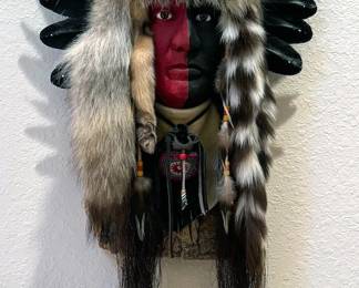 Mask figurine mounted on wood plank with horse hair, coyote pelt + crow feathers