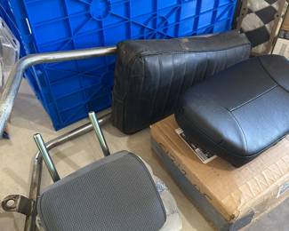 The gray headrest at the bottom of the photo is brand new. The black seat to the right is sitting on top. It’s Harley Davidson‘s original box. in the back of the picture is a backrest for a motorcycle.