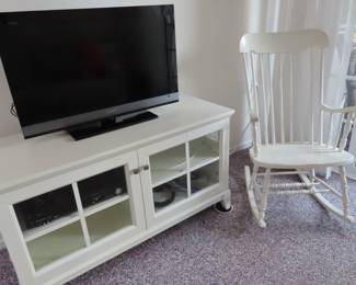 White rocking chair and white TV stand with media storage.