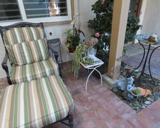 Heavy patio chair and footstool, mesh wire and iron side tables, plants and yard decor.