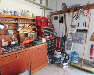 Work bench filled with tools, cordless leaf blower, shop vac, garden tools, paints, cleaners, nails, screws and saw horses. 