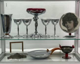 Top shelf: Farberware Bros Art Deco chrome cocktail glasses, vase, and nude figure stem compote candy dish with glass insert, an Art Deco circular picture frame. Lower shelf: A French cast metal picture frame, an Art Deco style "silent butler" and a Napier Art Deco silver plated olive bowl with Bakelite cherry cocktail sticks