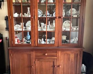 Ethan Allen American Impressions Cherry China Two Pc Lighted Cabinet--The lower piece features a drawer, one small cabinet, and two cabinets with an adjustable shelf. The higher piece features three glass and wood cabinet doors, lighting in the ceiling, and three adjustable glass shelves. The drawer features dovetail joinery. Minor wear from use; hutch is in good condition.