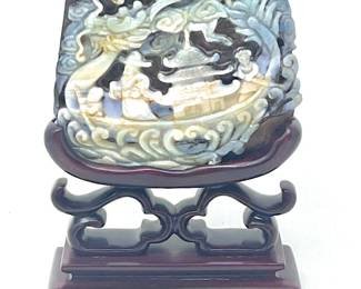 LOT 41 Register: www.woodardlipe.com CARVED FIRE OPAL IN THE FORM OF A DRAGON BOAT ON ROSEWOOD STAND Height 4 in., width 4 in., depth .75 in., Deeply carved dragon boat design on alluvial formation of opal with prominent signature on reverse.