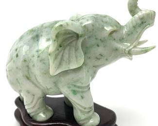 LOT 51 Register: www.woodardlipe.com HONAN JADE CARVED ELEPHANT IN WHITE AND GREEN ON ROSEWOOD BASE Length 3.75 in, width 2 in, height 4 in. Weight 333 grams with stand. Honan jade (hard stone) elephant with uplifted trunk indicating good luck and fortune, while the jade stone is revered for its symbolism of purity, harmony and protection.