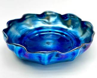 LOT 140 Register: www.woodardlipe.com LOUIS COMFORT TIFFANY (UNITED STATES 1848-1933) FAVRILE BOWL C. 1908, SIGNED Diameter 7.25 in, height 1.75in. Hand Blown glass bowl, with distinct embellished scalloped (10) edge. Rich blue green dichroic luster, similar to tetraisopropyl titanate, apparent on entirety of interior and exterior surface. Hand signed Favrile and initialed L.C.T. Produced at Tiffany Furnaces, New York. Pontil mark has been ground and polished. Condition: Very Good, with no apparent chips or defects of any kind. Very light surface abrasion in center of bowl, wear commensurate with age.