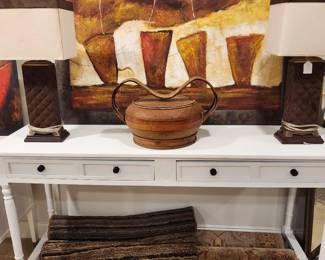white sofa table with rwo rugs underneath, lamps and antique basket on top