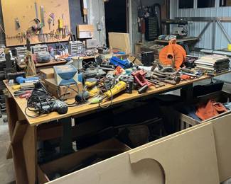 The central table has a lot of various powered and unpowered tools on it.  There are jigsaws, sanders, a biscuit cutter, several 90 degree clamps, powered router bits, extension cables, and more.