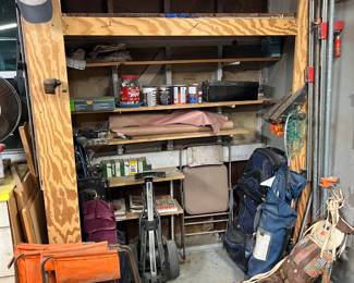 In this garage corner, there are a couple sets of golf clubs, a very large duffel bag, and a few long clamps hanging on the wall.  The tub on the floor contains a collection of woodworking magazines.