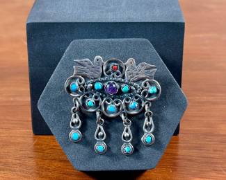 A stunning Taxco brooch or pendant with sterling silver, Turquoise, Amethyst, & Coral. Marked on the back, “Mexico 925″ with maker’s mark as shown in photos. This brooch measures 2” H x 2.25” W. Includes a loop on back to use as a pendant or a pin to display as a brooch. Total approx. weight is 26.10 grams.