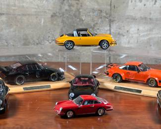 This lot features a total of 7 Porsche model cars by various makers including Bburago, Norev, & Exoto. All appear to be in very good condition and two Porsche’s include a display stand and cover. The two Porsche’s in the displays are 1976 Porsche 934 RSR & a 1976 Porsche 935 Turbo.