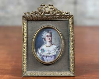 An antique French signed miniature portrait in gilt frame, circa 19th century. Signature present on right side of portrait as shown in photos. Likely from the Victorian era, this antique French portrait miniature features a young woman beautifully painted and covered with glass. The miniature is elegantly framed in an ornate gilt frame complete with an easel stand for tabletop display and measures in frame, 5” H x 3.5” W.
