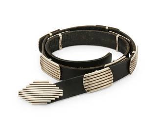196
A Southwest sterling silver concho belt
Late 20th century
Buckle marked with engraved pictograph of mountains and birds
A modernist-style belt with ribbed sterling silver elements including a stepped diamond-shaped buckle and eight oval ribbed silver conchos, all mounted to a black leather strap.
Buckle: 1.75" H x 3.125" W; each concho: 1.375" H x 2.25" W; belt: 42.25" L x 1.25" H
488.9 grams gross
Estimate: $700 - $900