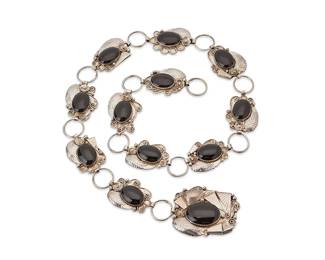 200
A Navajo sterling silver and onyx linked concho belt
Mid/late 20th century
Stamped: RH / Sterling [possibly Randy Hoskie, Diné]
A sterling silver link belt with a large buckle and eleven link conchos, each with elaborate floral, foliate, and feather silver overlay motifs, and each with a large bezel set oval onyx cabochon
Buckle: 2.5" H x 3" W; each concho: 1.5" H x 2.25" W; belt: 39.5" L
318.6 grams gross
Estimate: $500 - $700