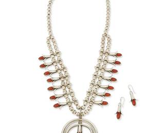 130
A Doris Smallcanyon Navajo sterling silver and coral squash blossom necklace set
Doris Smallcanyon (b. 20th century, Diné)
Late 20th century
Stamped: D. Smcyn
Featuring a three-wire naja with bezel-set coral cabochons set to three sculptural blossoms, with fourteen further set coral squash blossoms, all suspended from two strands of silver beads, with a pair of matching earrings, 3 pieces
Necklace: 25" L x 3" H; earrings: 1.5" H
105.7 grams gross
Estimate: $1,000 - $2,000