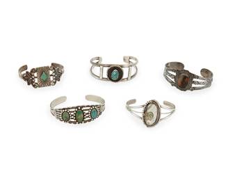 251
A group of Fred Harvey-style Southwest silver and set stone cuff bracelets
Mid-20th century
Five works:

Ralph Tawangyaouma (1894-1972, Hopi)
A Hopi three-wire cuff with set petrified wood stone
Stamped with artist's storm/thundercloud pictograph
An elaborate cuff with oval petrified wood cabochon, extensive stampwork and applied silver accents
6.125" inner C x 1.125" H, with a 0.875" gap

Four Southwest silver and stone set cuffs
One marked for sterling
Comprising a two-wire cuff with central set turquoise, a five-wire cuff with three set turquoise plaques, an ornate silver and diamond-shaped set turquoise cuff, and a delicate three-wire cuff with set mother-of-pearl cabochon, 4 pieces
Largest: 6.25" inner C x 1" H, with a 1.125" gap; smallest: 5.75" inner C x 1.25" H, with a 1.25" gap

5 pieces total
111.6 grams gross
Estimate: $200 - $400