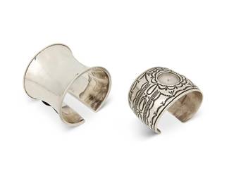 247
Two sterling silver cuff bracelets
Late 20th century
Two works:

Suzie James (1954-2012, Diné)
A Navajo sterling silver watch cuff bracelet
Stamped: Suzie James / Sterling
A slightly tapered cuff with bands of elaborate stampwork to each terminal, and a central opening featuring an associated "Liberty 1911" watch
6.75" total inner C x 2" H, with a 1" gap

A modernist-style sterling silver cuff
Stamped: 925
A tall shaped gauntlet cuff with folded terminal details
7" total inner C x 2.375" H, with a 0.75" gap

2 pieces
168.7 grams gross
Estimate: $200 - $400