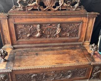 Italian Renaissance wooden carved bench with storage. Ornate Backrest: The top section showcases an elaborate crest with cherubs, scrollwork, and a central shield. Intricate Panels, Seating area, with storage