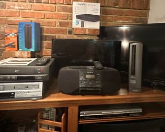Fire Stick w/ Alexa Voice Remote; Echo; Capello Compact DVD Player; Sony Boom Box CFD-533; Lasko Fan; Samsung Flat Screen 32in; Zenith VCR VRM4120; Sansui VCR/DVD Combo Platinum Plus; Remotes; DVD/ Blu-Rays/ VHS Tapes; Power Strips; Koss Progressive Scan Slim DVD Player; Polaroid 15" LCDTV Cabinet Mount TV; CD's, Cassettes, Albums, 45 Records; Sport AM/FM Cassette Player with Lantern; Panasonic One Touch Recorder RQ-339; Starlite 4.5" Black & White Portable TV