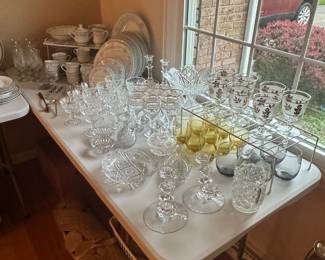 There are two banquet tables in the living room filled with glassware and China