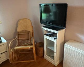 There’s a nice wicker hamper. The television is on a nice little, but seems to be a bathroom cabinet and a beautiful wicker rocker.