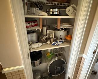 This closet in the kitchen is filled with small kitchen appliances and accessories