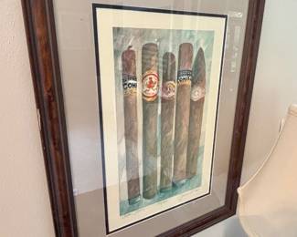 The image shows a framed, limited-edition print titled "Arfan Gems" by Grone Doll, numbered 148 of 500. It depicts a collection of cigars with recognizable brand labels. Key details include:
Subject: The artwork features five cigars, each with a distinct brand label: COHIBA, HOYO DE HABANA, and COHIBA.
Artist and Title: The print is signed "Grone Doll" and titled "Arfan Gems."
Edition: It is a limited edition print, number 148 out of 500.