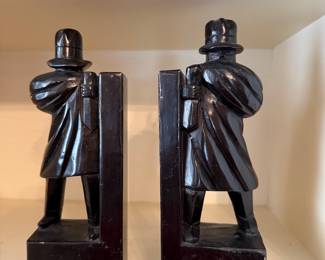 The objects are a pair of Art Deco bookends depicting figures in coats and hats, likely dating from the 1920s or 1930s.
