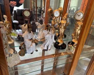 Antique ceramic/porcelain figurines and gold-colored clocks with visible pendulum and Roman numerals and a wooden-cased clock