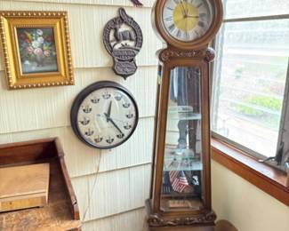 Freestanding Grandmother’s Style Clock with carved details and glass shelving with mirrors. Also pictured are a civilian/military clock, a metal John Deere wall hanging, a flying eagle wall hanging in American flag colors, and a golden framed vintage rose flower picture.