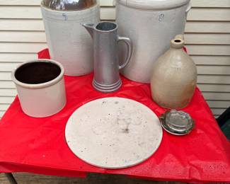 Collection stoneware crocks and jugs originally used for storing liquids. Also pictured is a tall metal pitcher.