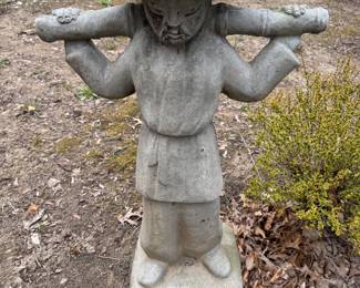 Concrete garden statue of figure carrying a pole on its shoulders. Asian-inspired design with decorative elements.