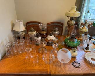 Collection of antique oil lamps and their components. Various glass chimneys, shades, and oil reservoirs in different sizes, shapes, and designs.