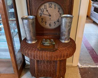 Oval Wicker end/accent table in beautiful condition. Also pictured are an antique carved wooden clock, 2 handcrafted aluminum vases with designs, and a hanging wood and metal eagle door knocker.