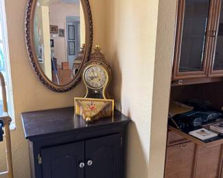 Small Ebony Cabinet with Swiss Mantle Clock and shelf. Gilt Wood Oval Mirror.