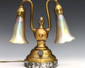 An early 20th century Bronze desk lamp with Tiffany Favrile glass shades. Double swan neck with floriform Gold Tiffany Favrile glass shades over a cast Bronze base with artichoke finial and Grey Saint Anne Marble foot. Shades signed "L.C.T." at fitters. Some wear to patina and slight pitting, small hole to casting at knop, tiny flakes to fitters. Shades are 4 1/4" high, lamp is 9" high overall.