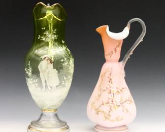Two late 19th century Victorian enameled Art Glass pitchers. Includes a Yellow to clear glass Mary Gregory pitcher with ruffled handle and figural courtship decoration, and a cased Pink satin glass ewer with lobed body and floral decoration. Minor surface wear and fleabites. Up to 14 1/2" high.